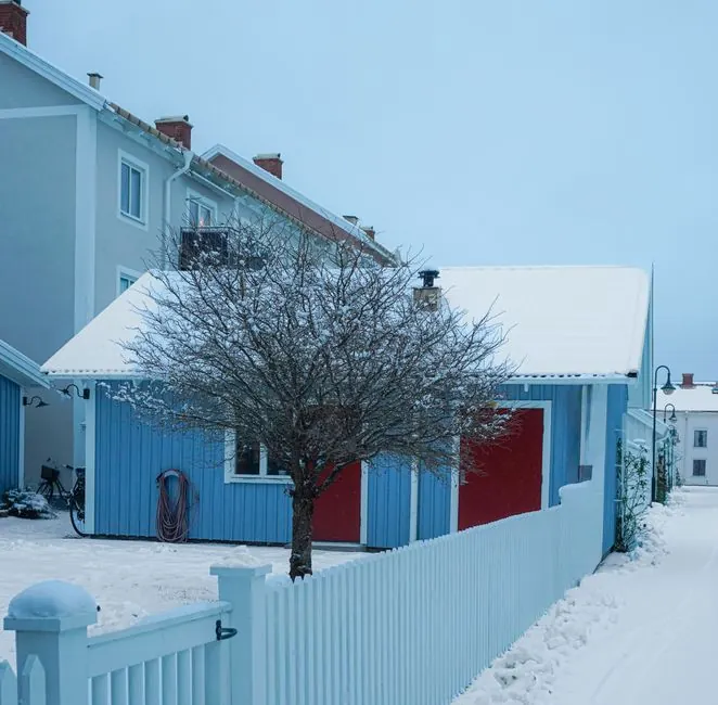 Charming blue house with red doors covered in snow, surrounded by a winter landscape.