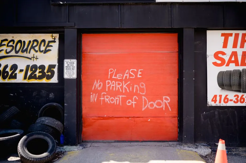 Red garage door with handwritten no parking sign surrounded by tire shop advertisements.